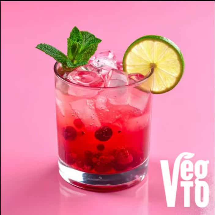Vegan cocktail with berries, mint, and lime on pink background.